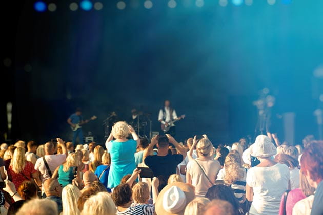 Rückansicht einer feiernden Menschenmenge bei einem Open-Air-Konzert, die Richtung Bühne gewandt stehen und Beifall klatschen