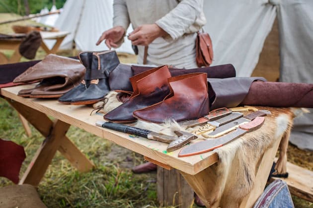 Fokus auf einen Tisch, auf welchem mittelalterliche Waren aus Leder, Lederschuhe, Messer und mehr zum Verkauf angeboten werden..