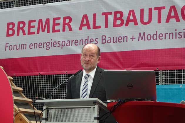 Ein Mann im Anzug steht bei der Messe der Bremer Altbautage auf einem Podium und hält einen Vortrag. 