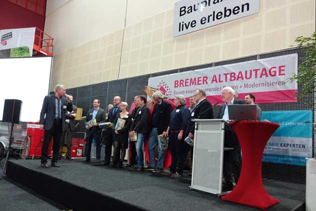 Mehrere Menschen stehen bei den Bremer Altbautagen beim Vortrag "Baupraxis live erleben" auf einem Podium.