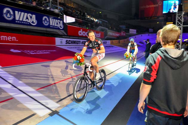Mehrere Rennradfahrer fahren bei den Bremer SIXDAYS auf einer Indoor-Rennradbahn an Zuschauern vorbei.