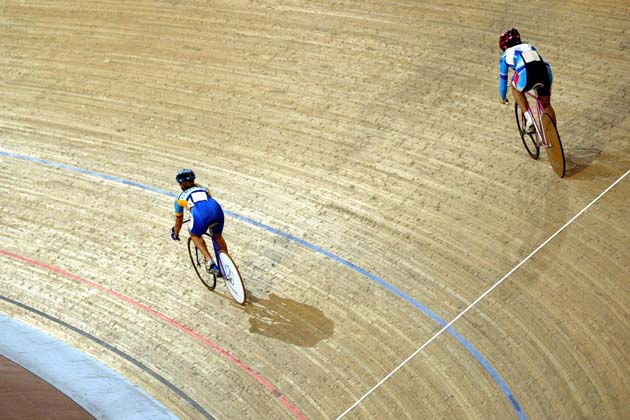 Zwei Rennradfahrerinnen fahren durch die Kurve einer Indoor-Rennradbahn.