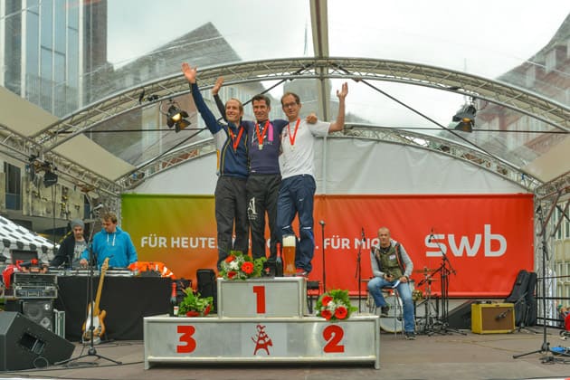 Drei Männer stehen als die ersten Drei beim swb-Marathon auf dem Marktplatz auf einem Podest.