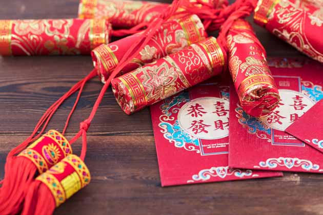 Traditionell chinesische Neujahrsdekoration sowie rote Umschläge liegen auf einem dunklen Holztisch.