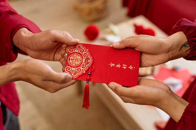 Gemäß der chinesischen Neujahrstradition übergibt eine ältere Person einen roten Umschlag an eine jüngere Person. 