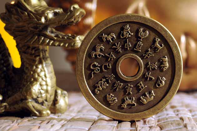 Eine goldene Drachenstatue und eine goldene Münze mit Loch in der Mitte. Auf der Münze sind die chinesischen Tierkreiszeichen als Bild und mit chinesischer Schrift abgebildet.