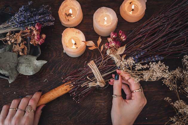 Eine Person schmückt den Tisch mit Kerzen, Sträuchern und Kräutern für das Fest Samhain aus dem Halloween entstanden ist.