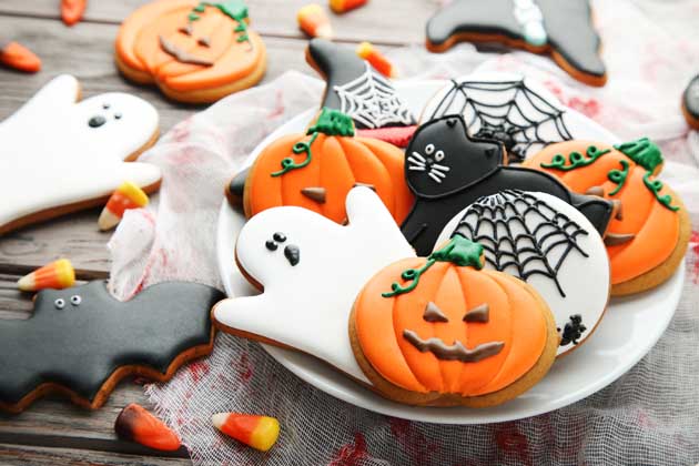 Kekse zu Halloween mit gruseligen Motiven stehen auf einem dekorierten Tisch.