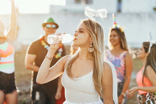 Eine junge Frau im Engelskostüm trinkt auf einem Festival aus einer Wasserflasche.