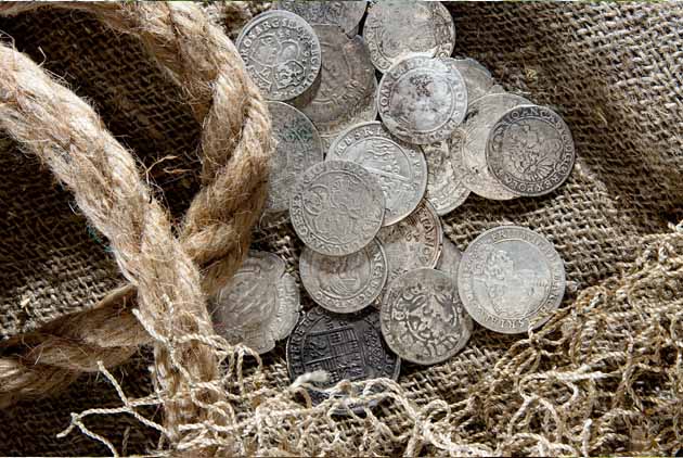 Silberne Münzen liegen auf altem Stoff und Garn.