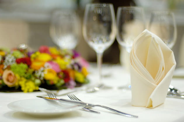 Ein schön gedeckter Tisch mit Teller, Besteck, Gläsern, Blumenkranz und gefalteter weißer Serviette.