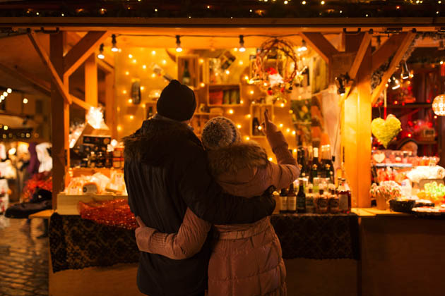 Sich umarmendes, glückliches Paar von hinten, das an einem Weihnachtsstand die Ware betrachtet