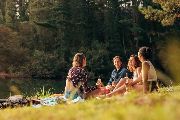Eine Gruppe von vier Freunden sitzt mit einer Picknickdecke am Seeufer