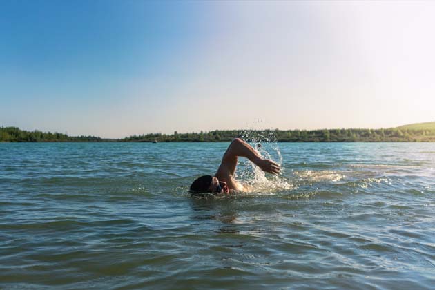 Mann mit Schwimmbrille krault in einem See im Sommer