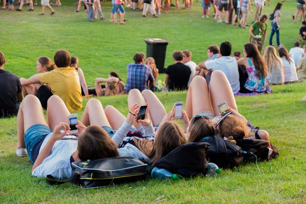 Vier Mädchen, die auf der Breminale am Deich im Gras liegen und auf ihre Smartphones schauen, während Sie der Musik lauschen