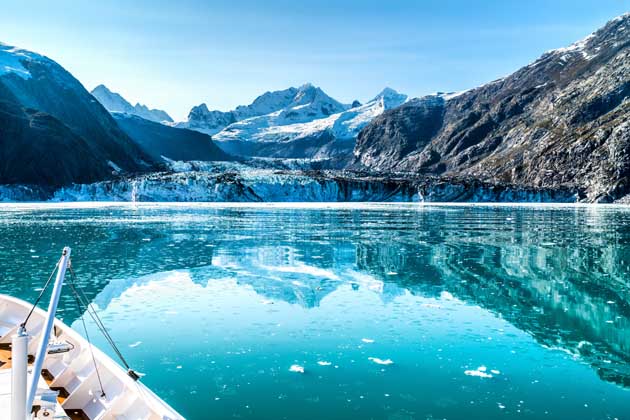 Ein weißes Boot fährt auf einem von Bergen und Gletschern umgebenen Eissee.