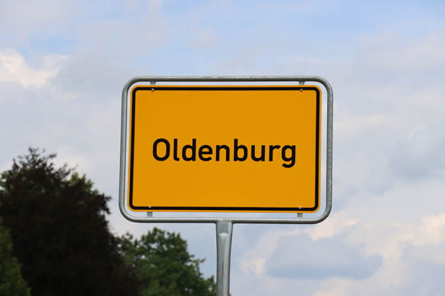 Das Ortseingangsschild von Oldenburg mit Baum und Himmel im Hintergrund.