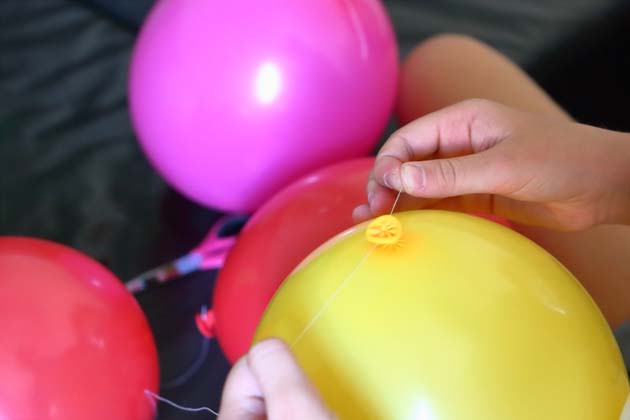 Um mehrere bunte Ballons wird ein Faden gebunden.