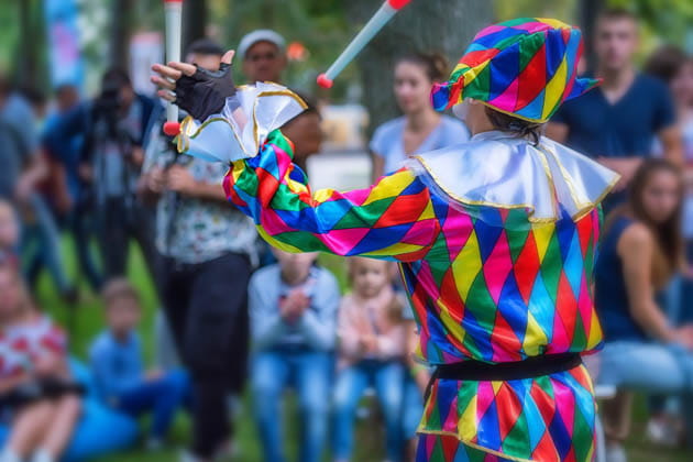 Bunt gekleideter, jonglierender Clown in Rückenansicht, der sein Publikum mit seiner Straßenkunst begeistert
