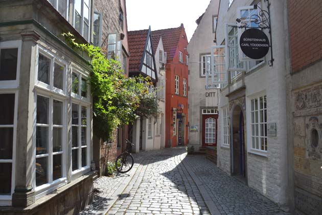 Lange, schmale Gasse im Schnoorviertel in Bremen mit kleinen dichtbebauten Häusern und Geschäften auf beiden Seiten, deren Schilder zu sehen sind.