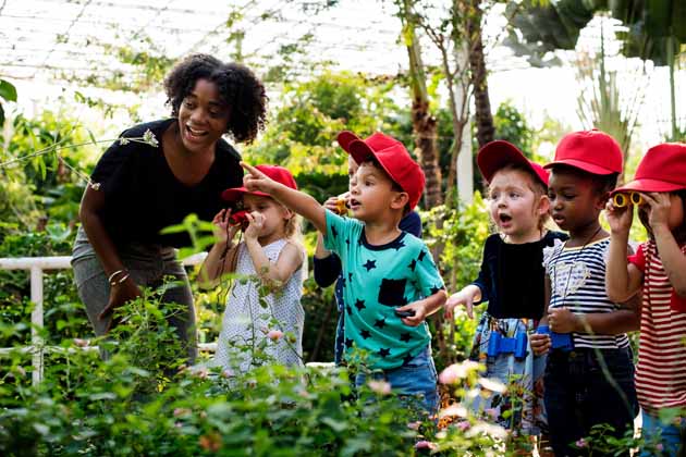 Eine Lehrerin zeigt einer Gruppe von kleinen Kindern die Pflanzenwelt in einem Gewächshaus.