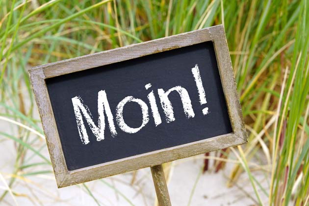 Ein Holzschild am Strand auf dem „Moin!“ steht.
