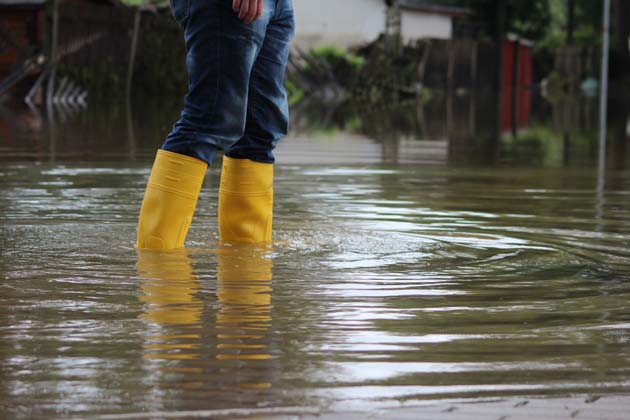 Eine Person steht mit Jeans und gelben Gummistiefeln im Hochwasser.