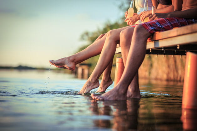 Mehrere Freunde an einem Sommertag hängen vom Steg aus ihre Füße ins Wasser.