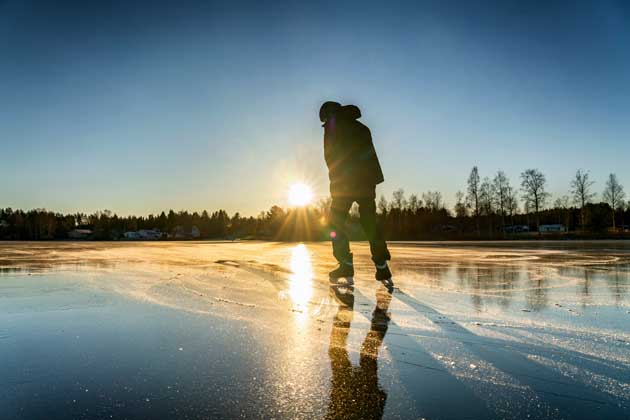 Eine Person fährt Schlittschuh auf einer Eisfläche, während im Hintergrund die Sonne untergeht.