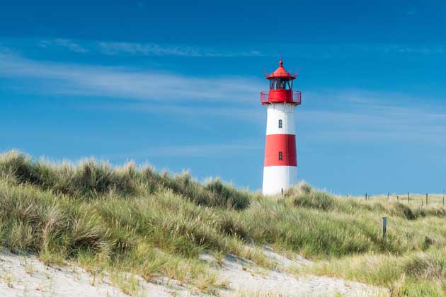 Ein rot-weiß gestreifter Leuchtturm steht an einer sandigen Küste an der Nordsee.