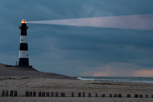 Ein Leuchtturm an der Küste am Strand strahlt bei Nacht ein Lichtsignal aus und dient als Leuchtfeuer.