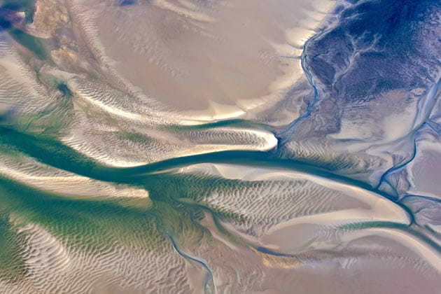 Luftaufnahme des Wattenmeers bei Ebbe mit sichtbaren Prielen und Wattströmen.