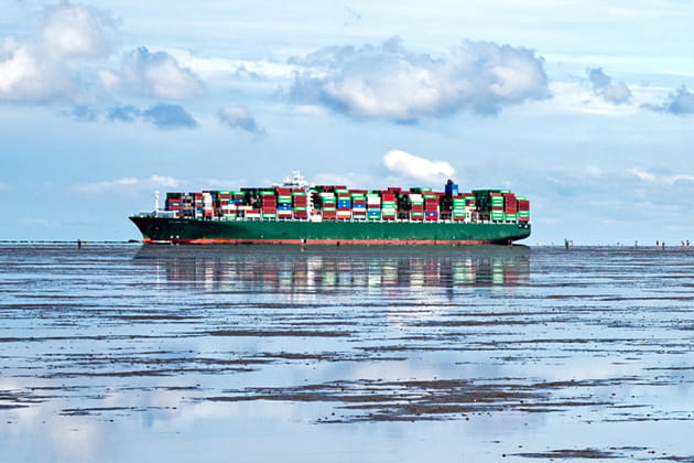 Ein Containerschiff voll beladen mit Containern auf offener See bei Sonnenschein.