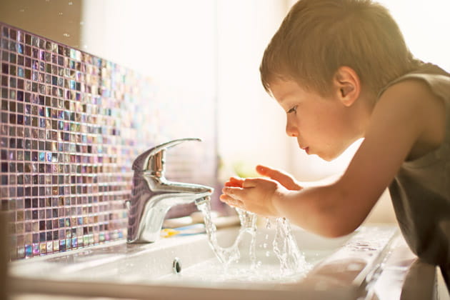 Ein kleiner Junge am Waschbecken, der Leitungswasser trinkt