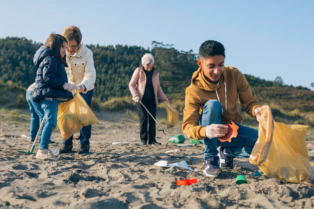 Kinder sammeln gemeinsam mit zwei älteren Frauen  in ihrem nachhaltigen Urlaub mit Plastiktüten am Stand Müll ein