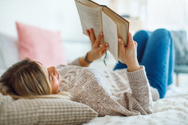 Auf dem Rücken liegende blondhaarige Frau, die im Bett ein Buch liest
