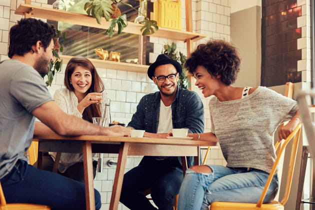 Vier junge Menschen, die in einem Repair Café an einem Tisch sitzen, sich unterhalten und Kaffee trinken
