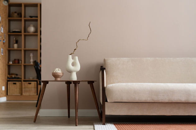Skandinavisch eingerichtetes Wohnzimmer im minimalistischen Stil mit beigem Sofa, Beistelltisch und Regal im Hintergrund 