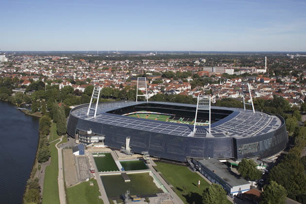 Der Blick von oben halbschräg über Bremen, im Vordergrund die Weser und das Weserstadion vor blauem Himmel