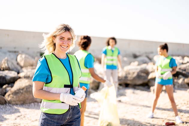 Gruppe von jungen Frauen in Warnwesten säubern mit Mülltüte und Handschuhen den Strand.