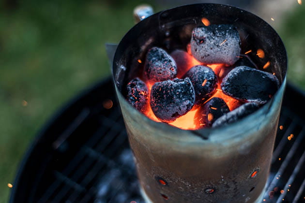 Ein Anzündkamin voller Ruß, gefüllt mit Glut und heißer Grillkohle, steht auf einem schwarzen Kugelgrill.
