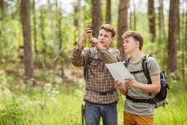 Zwei junge Männer sind mit Rucksäcken im Wald suchen das GPS-Signal fürs Geocaching.