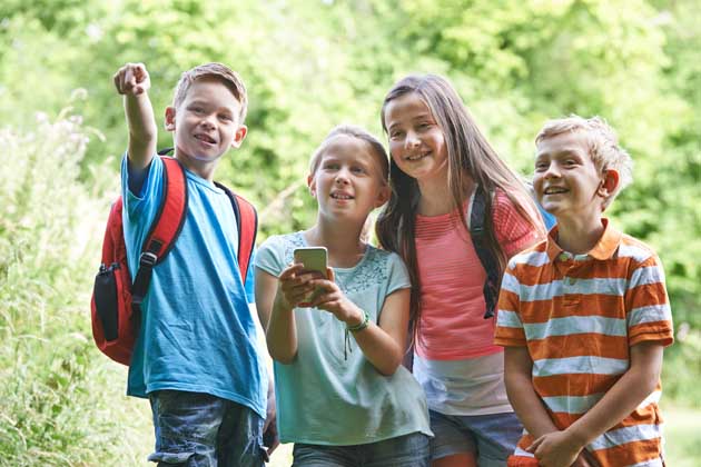 Vier Kinder haben Spaß bei der Suche nach einem Geocache mit dem Handy.
