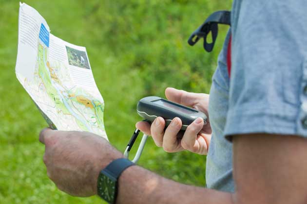 Eine Person mit blauem Hemd sucht mit GPS-Empfänger und Landkarte nach einem Geocache.