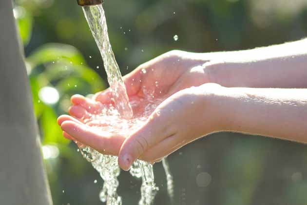 Eine Person hält zwei Hände unter einen laufenden Wasserhahn, um das Wasser aufzufangen.
