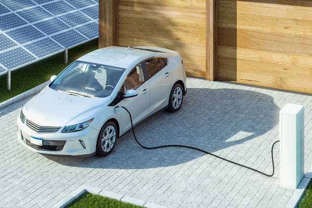 Elektroauto, das an einer Elektrotankstelle aufgeladen wird, mit Solarzellen im Hintergrund