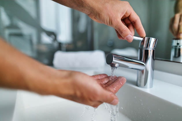 Eine Person hält ihre Hand unter den Wasserhahn und dreht ihn auf, um die Temperatur zu testen. 