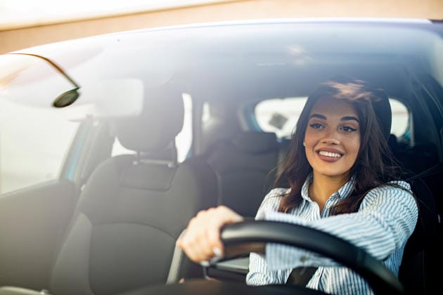 Lächelnde Frau mit Bluse sitzt hinterm Steuer im Auto.