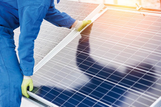 Eine Person im blauen Anzug mit hellen Handschuhen befestigt ein Solarmodul von einer Photovoltaik-Anlage.