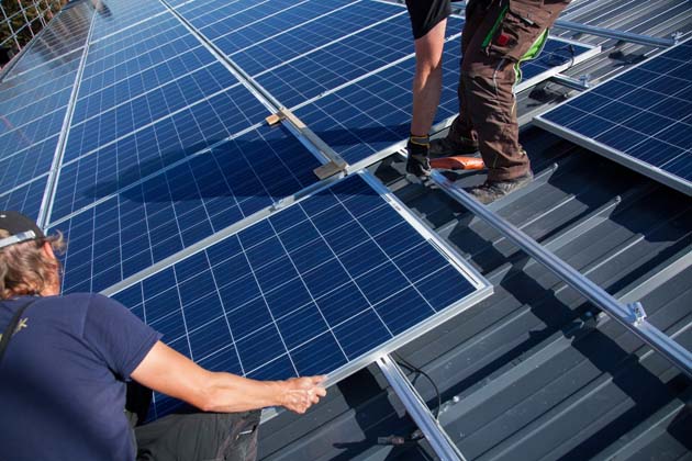 Zwei Monteure installieren für Photovoltaik mehrere Solarmodule auf einem Dach.